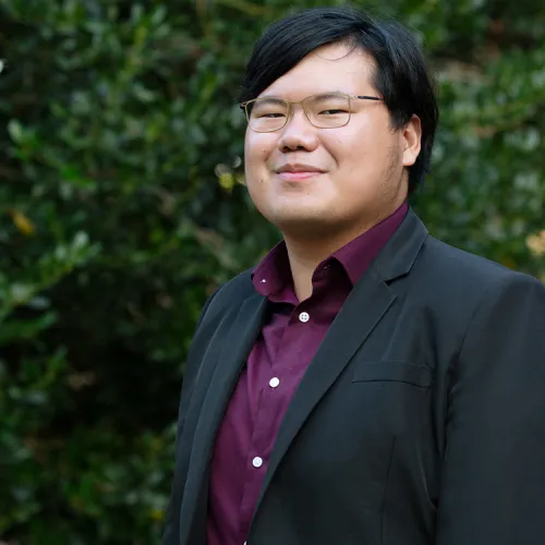 Tzu Kuang Tan stands in front of lush greenery.