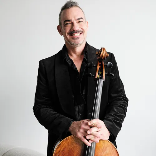 A headshot of Joshua Gindele in formal black concert attire with his cello