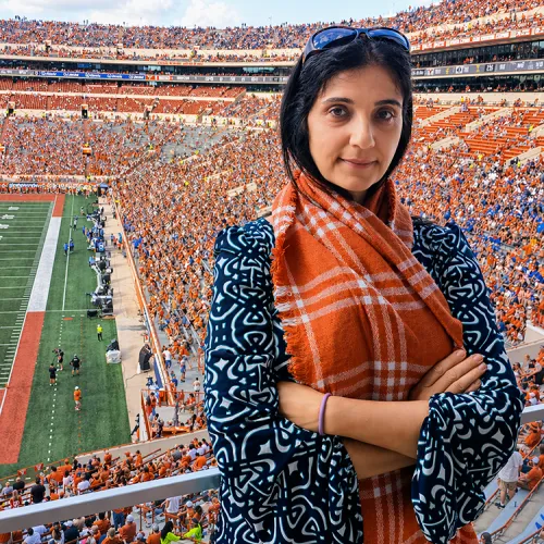 Anna Piatagorsky stands with arms confidently folded and looks at the viewer, behind her is a packed UT football stadium.