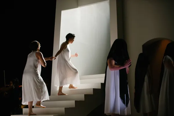 Two nuns wear only their undergarments. One leads the other up a staircase toward a bight white light, as if ascending into heaven.