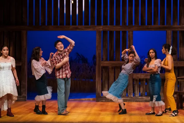 performers dance inside a barn set, during a party scene.