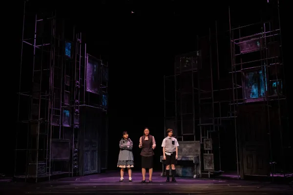 three performers stand center staged, dwarfed by a an expansive, ghostly gothic set