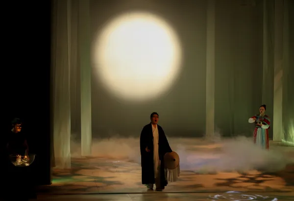 A shadowy figure stands at the center of a fog-filled stage, with a soft glowy moon in the background.