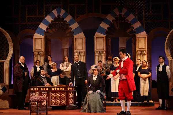 The cast of Figaro gather together on stage singing around a seated woman who looks unhappy 