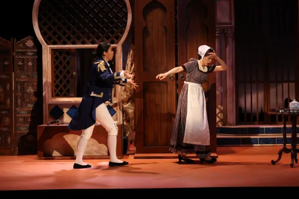 A woman in a maid's uniform pulls away from a man who chases after her, she looks distraught.