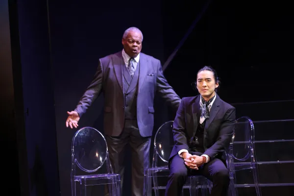 Two men dressed in 3-piece suits sing somberly on stage