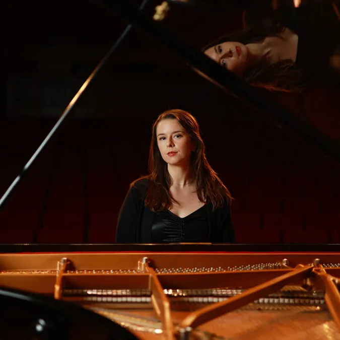 Maria Parrini sits at a piano and looks confidently into camera.