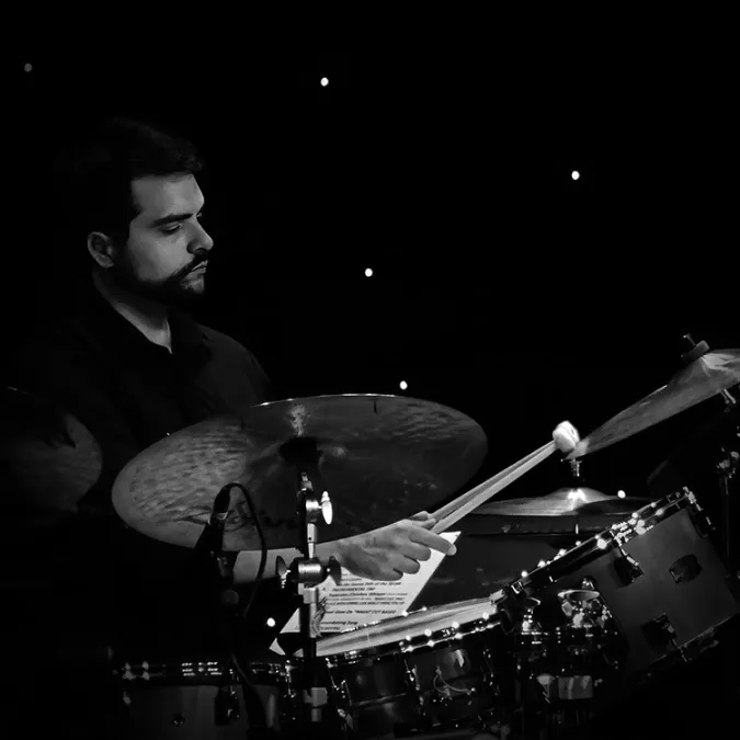 Daniel Dufour hitting a cymbal on his drum set with a pair of mallets. 