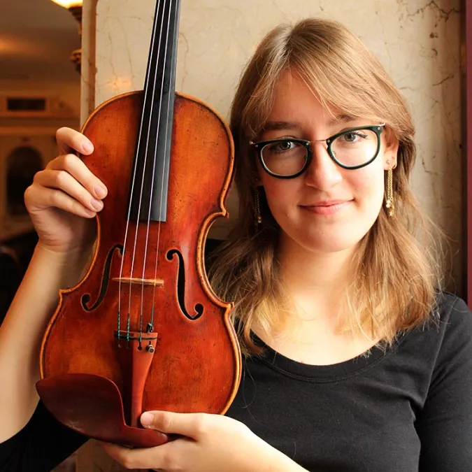 a Headshot of Chloe Yofan, sitting in a casual spot, holding up her violin 