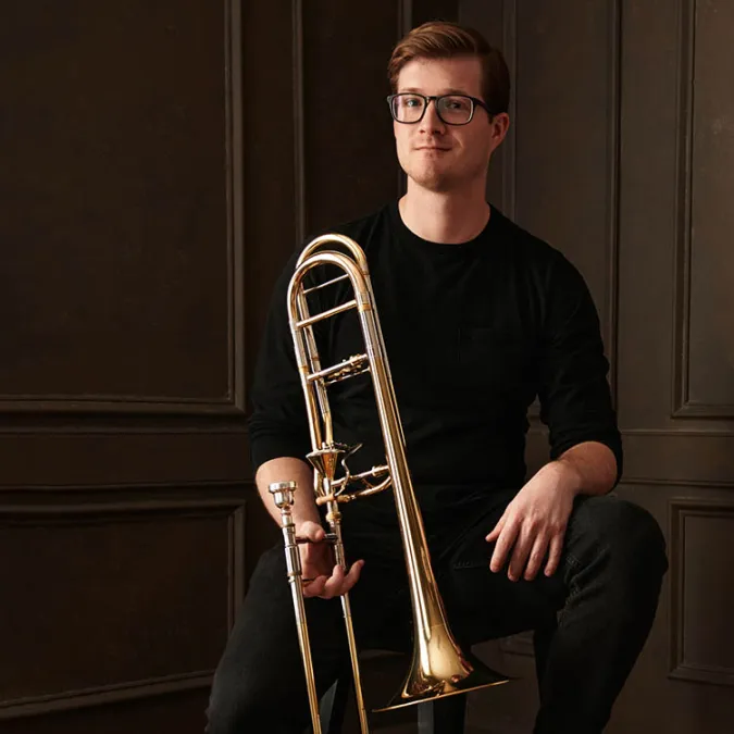 A headshot of Evan Williams, sitting on a stool with his trombone.