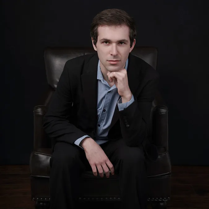 a headshot of Aaron Kurz sitting in a leather chair in a darkly lit room.