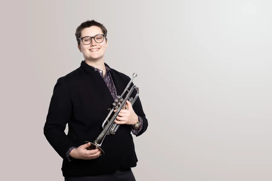A trumpet player holds her trumpet and smiles