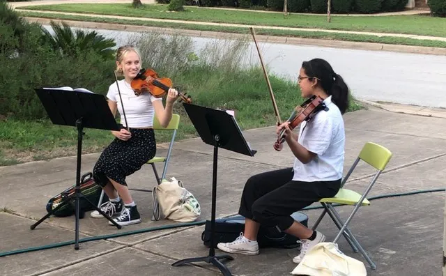 Lucy Hamre (left) and Ileana Nicholson (right) share a knowing look as they preform their violin arrangements for a socially-distanced audience.