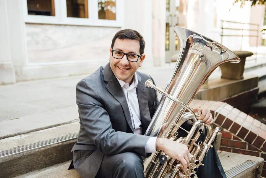 Benavidez sits on stairs outside a building with his tuba on his lap.