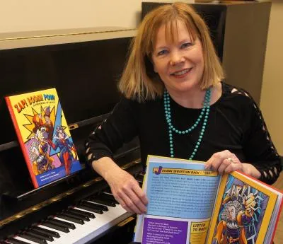 Lucy Amen Warner holds a copy of her children's book while sitting at a piano
