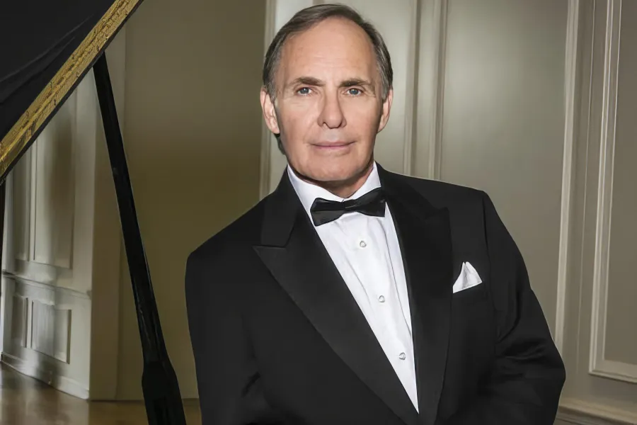 Pianist James Dick leaning on a piano in a tuxedo