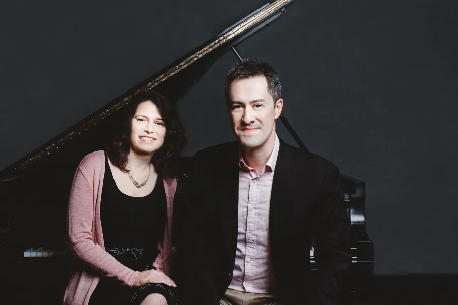 Pianists Patti Wolf and Andrew Brownell side side by side on a bench in front of a grant piano.