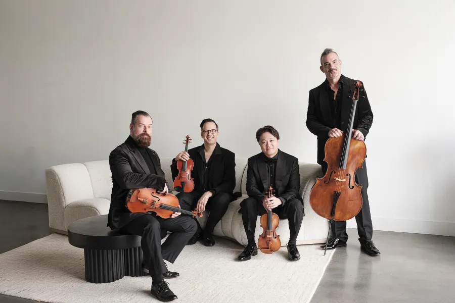 The Miro quartet pose in all-black with their instruments, against a white couch and wall