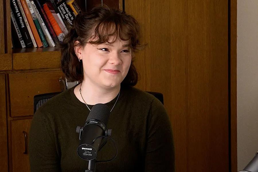 Sidney Becktold talking into a mic with a bookshelf in the background