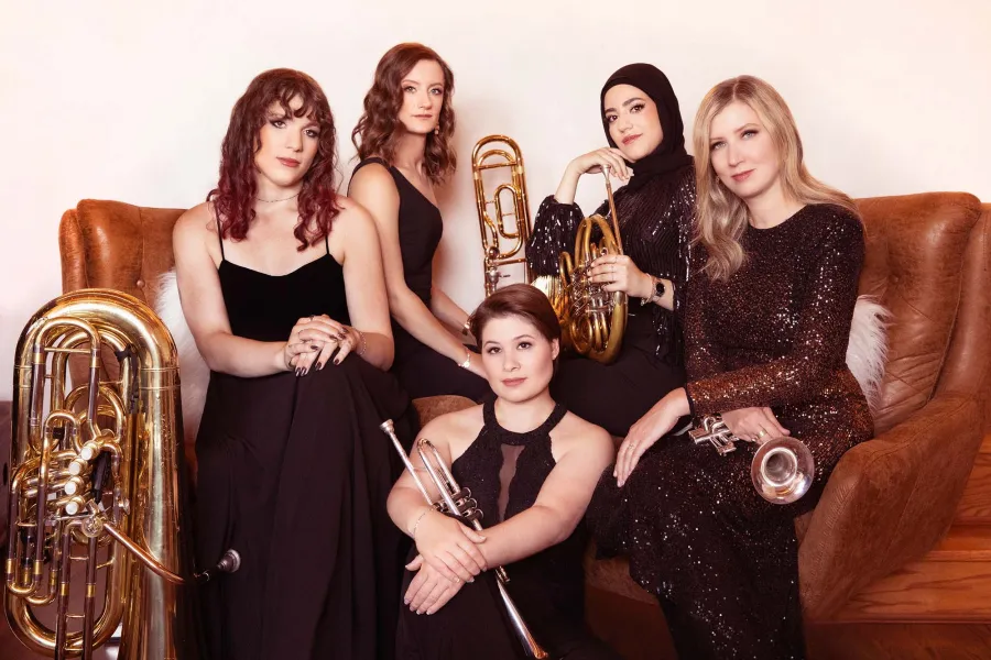 Seraph Brass sit together on and around a leather sofa, with their instruments close at hand. 