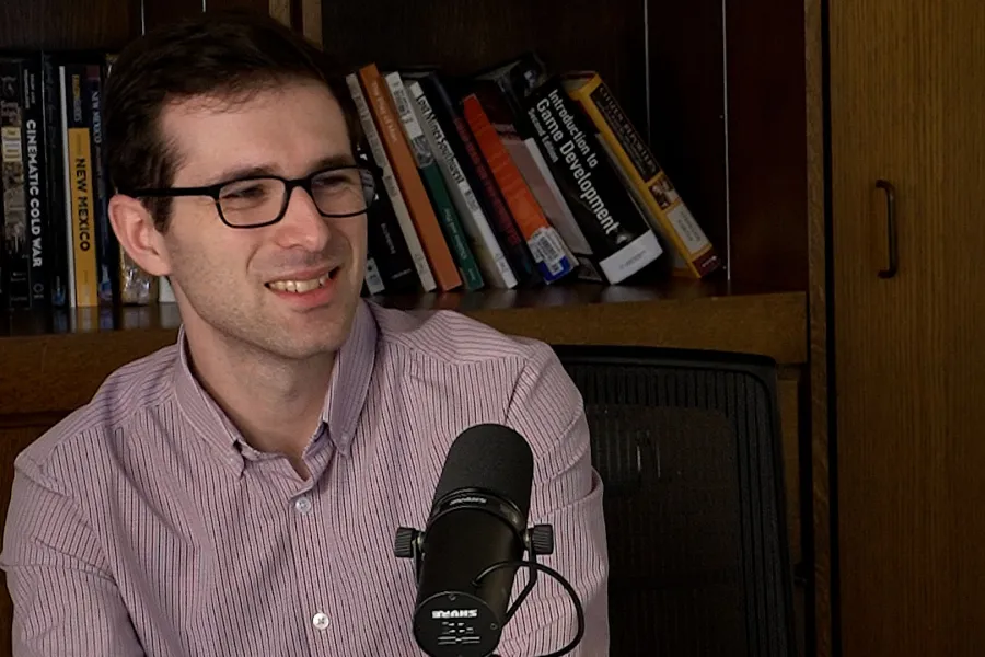Man talking into a mic with a bookshelf in the background