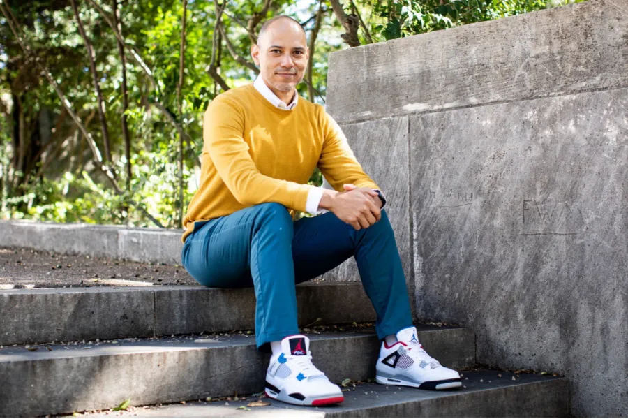 Charles Carson sitting in a garden with a sweater, blue jeans and tennis shoes on