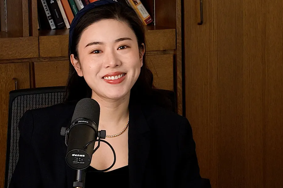 Jinni Shen talking into a mic with a bookshelf in the background