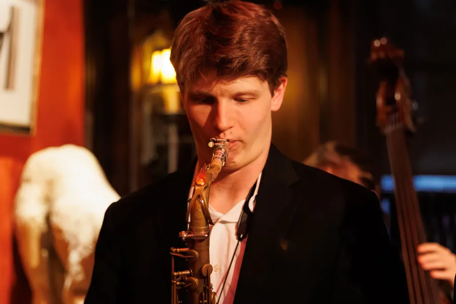 Eli Wyatt playing a saxaphone with a bass player in the background