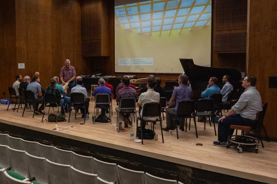 A group of adult students listen to a speaker on a stage