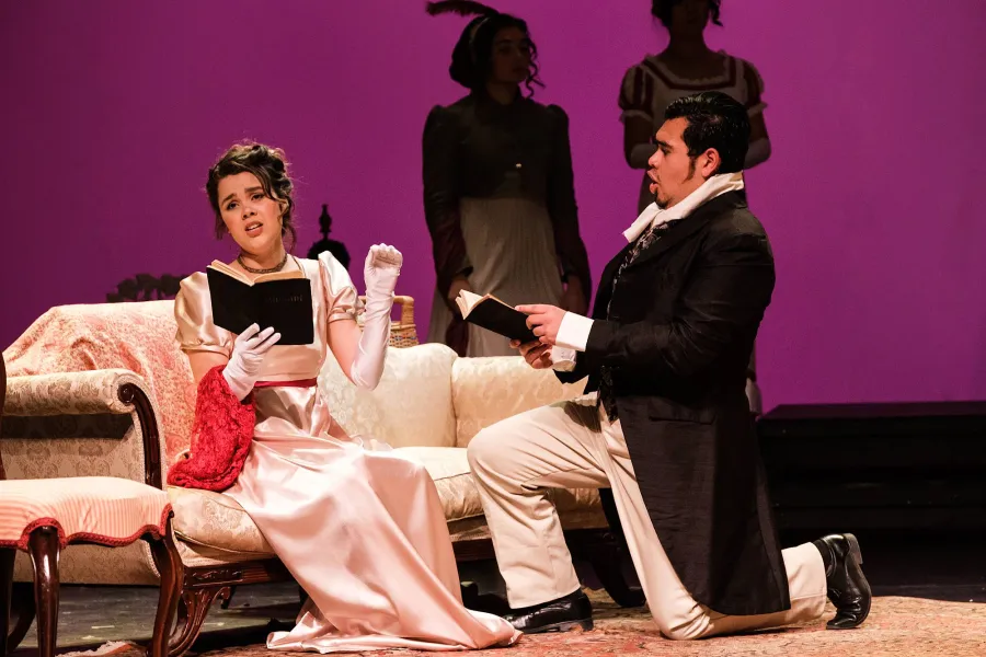 A woman leisurely reads on an ornate sofa, while a man kneels at her side, also with an open book in hand.