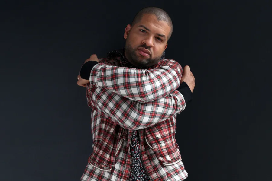 Jazz pianist Jason Moran hugs himself wearing a red and white plaid blazer.