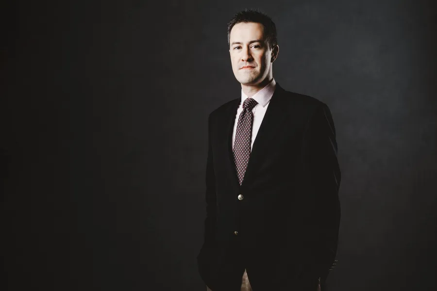 A portrait of pianist Andrew Brownell wearing a black suit and a pink shirt.