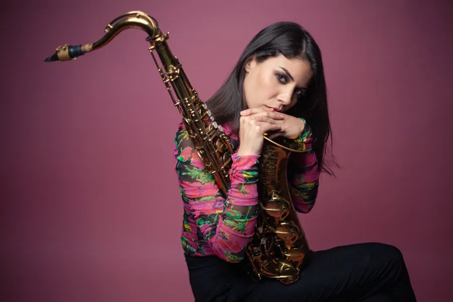 Melissa Aldana sits for the camera, holding her tenor saxophone.