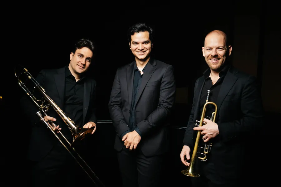 Portrait of the members of Triple Cortado in black suits holding their instruments.