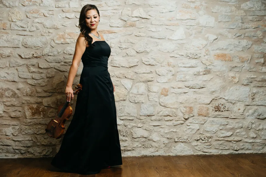 Violinist Sandy Yamamoto holds her violin wearing a black strapless gown.