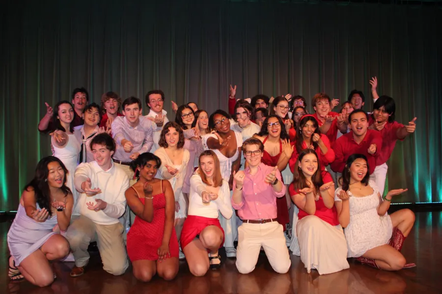 Members of the Longhorn Singers smile and gesture toward the camera, gathered on stage in front of a curtain.